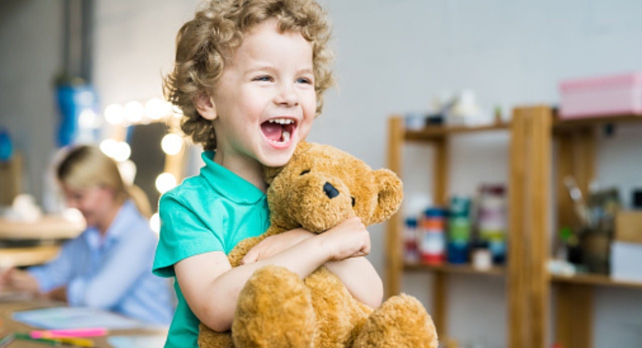 Criança sorrindo e abraçando ursinho, ilustrando a importância de saber como lavar bichinho de pelúcia e mantê-lo limpo.