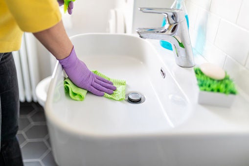 Pessoa limpando a pia do banheiro com produtos certos, garantindo uma limpeza segura e eficiente, sem depender de misturinha para lavar banheiro.