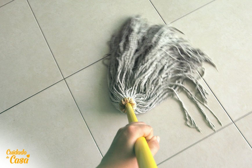 Esfregão branco passando sobre o piso para fazer a limpeza de chão