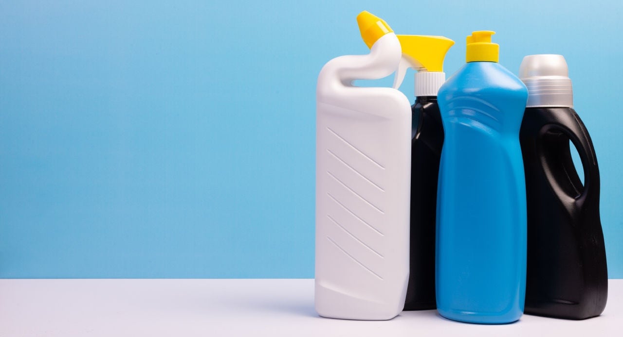 Quatro frascos variados de produtos de limpeza sobre fundo azul, ilustrando diferentes tipos de desinfetante.