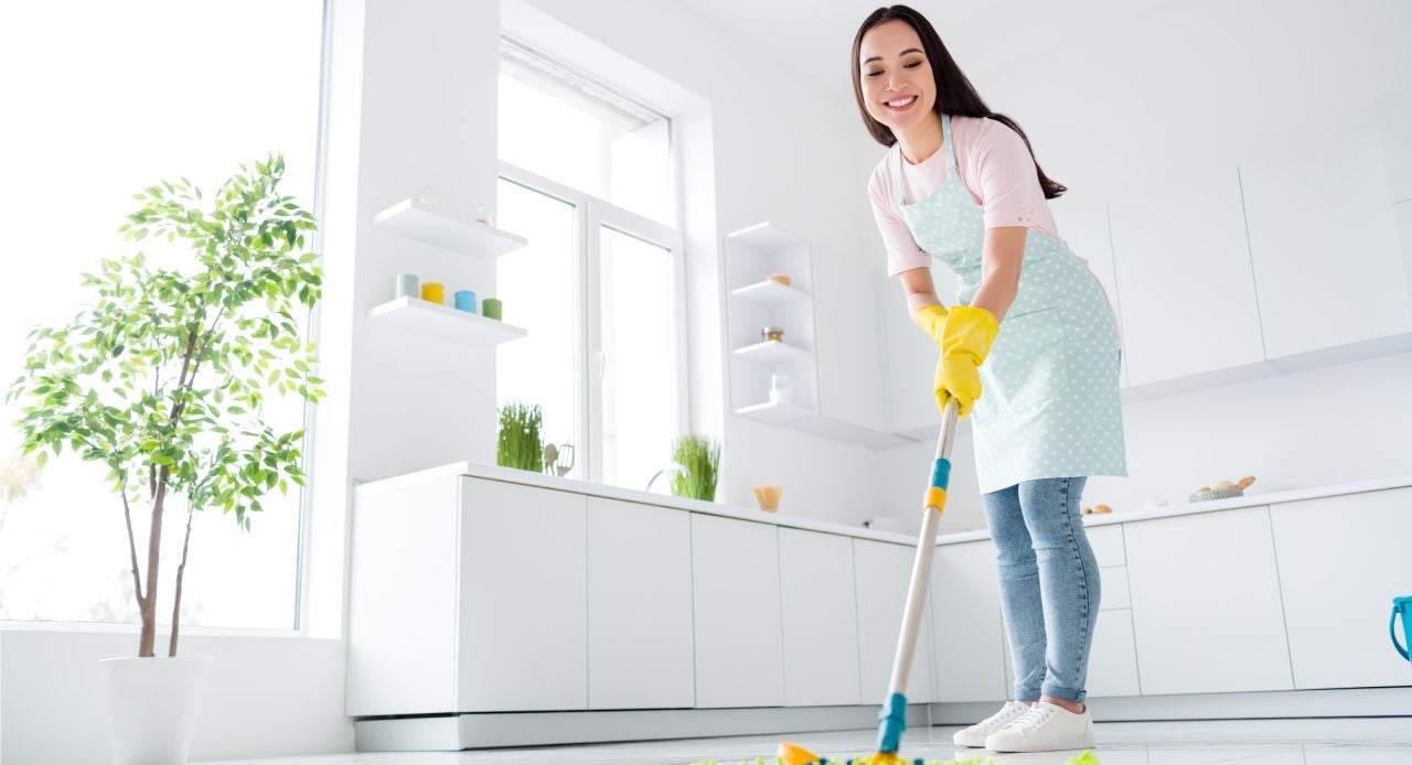 Mulher usando um limpador de porcelanato no piso da cozinha de casa, com ajuda de um mop de microfibra.