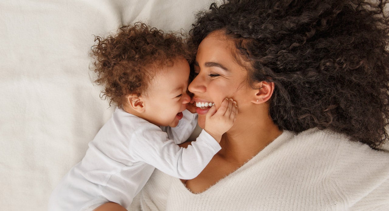 Mamãe deitada na cama com seu filho após lavar suas roupas com sabão para roupa de bebê.