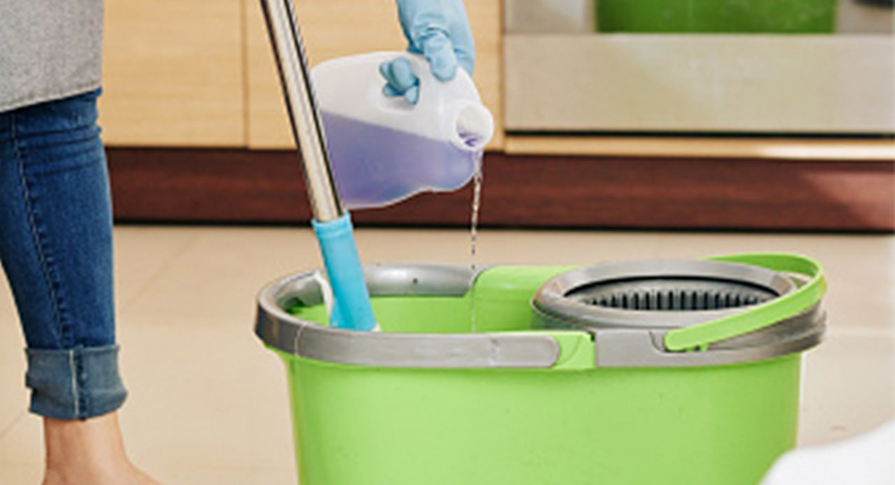 Pessoa diluindo o desinfetante concentrado no balde de um mop giratório para limpar a casa