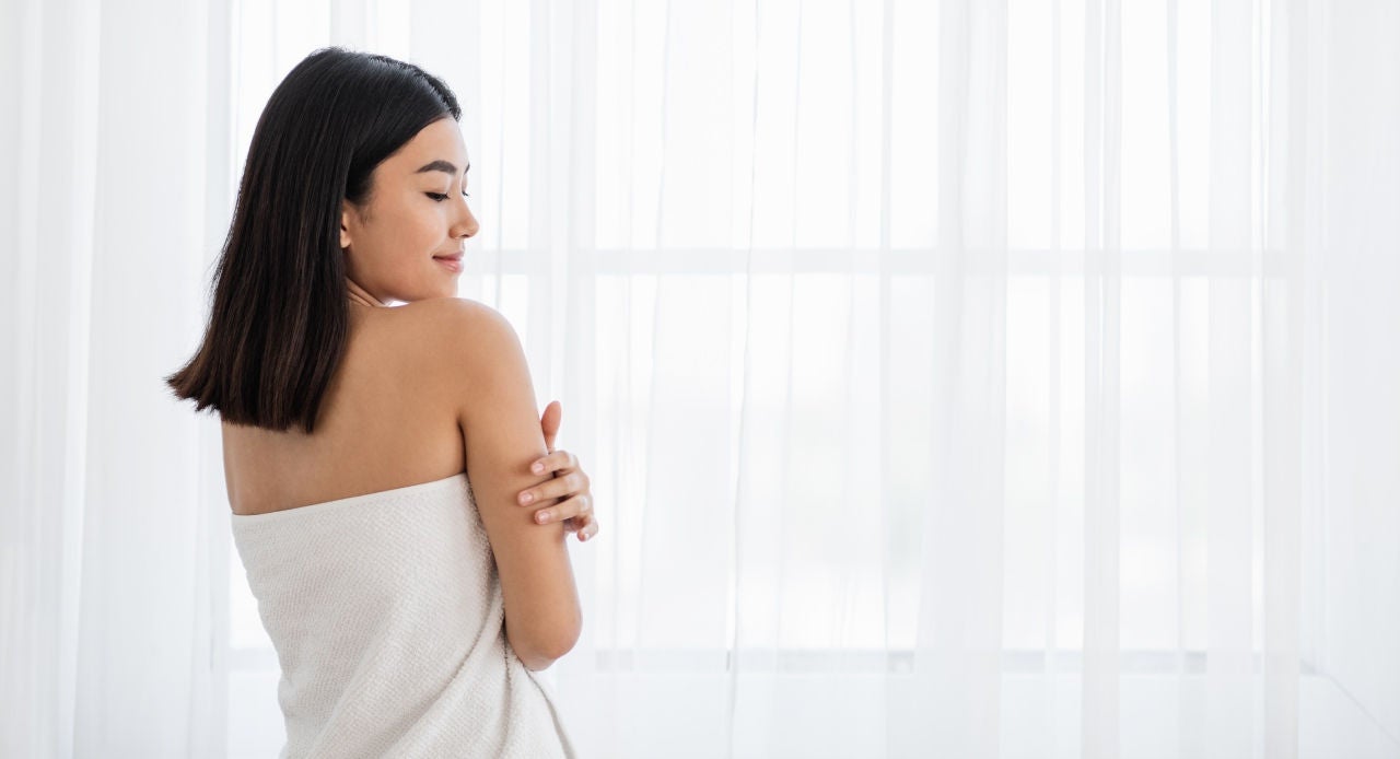 Mulher com uma toalha enrolada em volta do corpo pensando em qual calcinha de renda usará