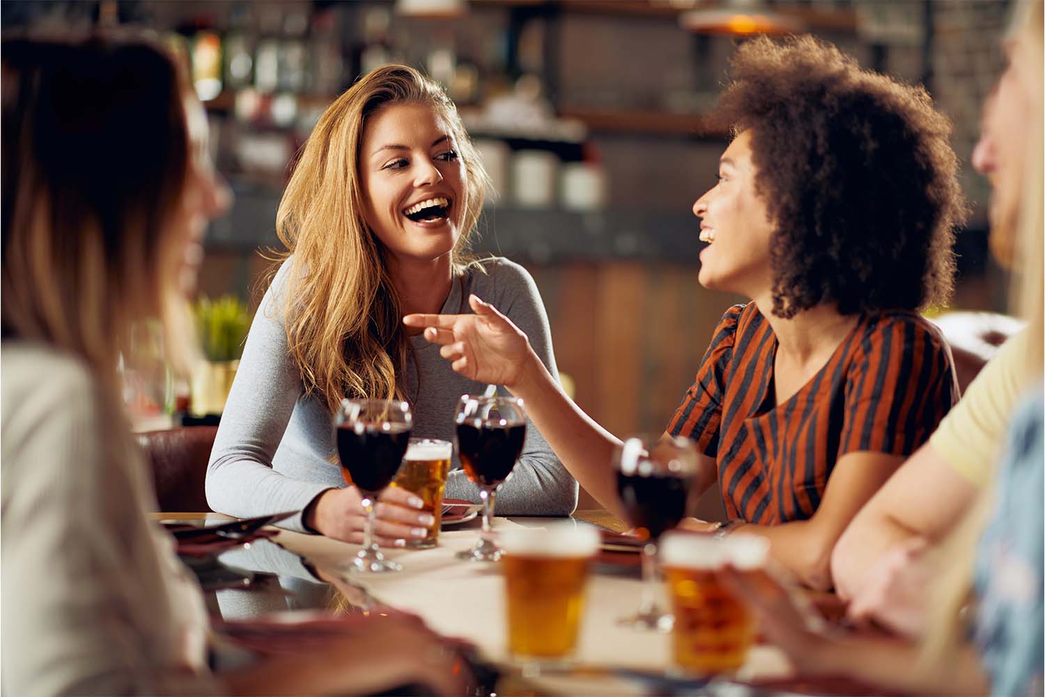 Grupo de amigas bebendo e sentadas à mesa prontas para  degustar uma tábua de frios