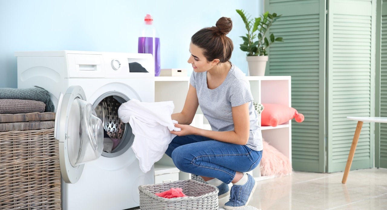 Mulher agachada em frente à máquina de lavar conferindo suas peças limpas e cheirosas depois de serem lavadas com o melhor desinfetante para roupas
