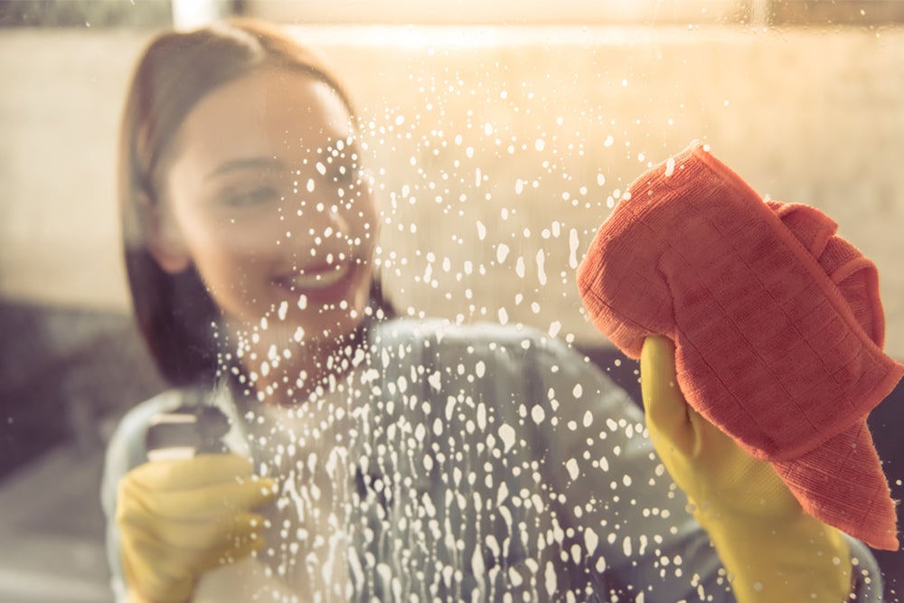 Mulher usando produto para limpar vidro na faxina de casa