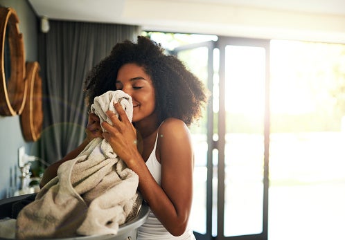 Mulher cheirando uma peça de roupa com um sorriso satisfeito, transmitindo a sensação de uma casa cheirosa e aconchegante. 