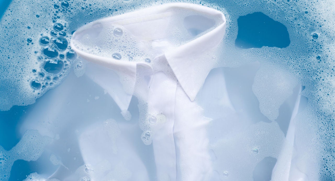 Camisa branca de molho em água com sabão, ilustrando como tirar mancha de molho de tomate da roupa.