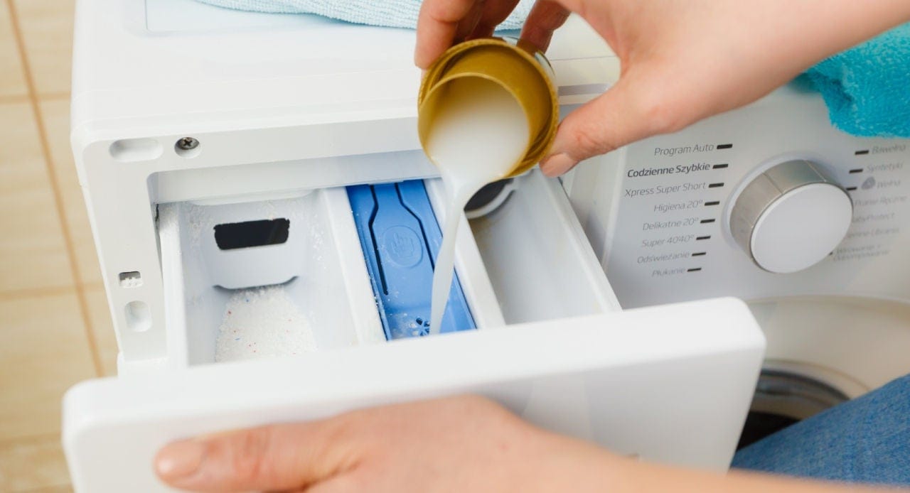 Pessoa colocando o melhor sabão líquido Ola no dispenser da máquina de lavar, garantindo roupas limpas e perfumadas.