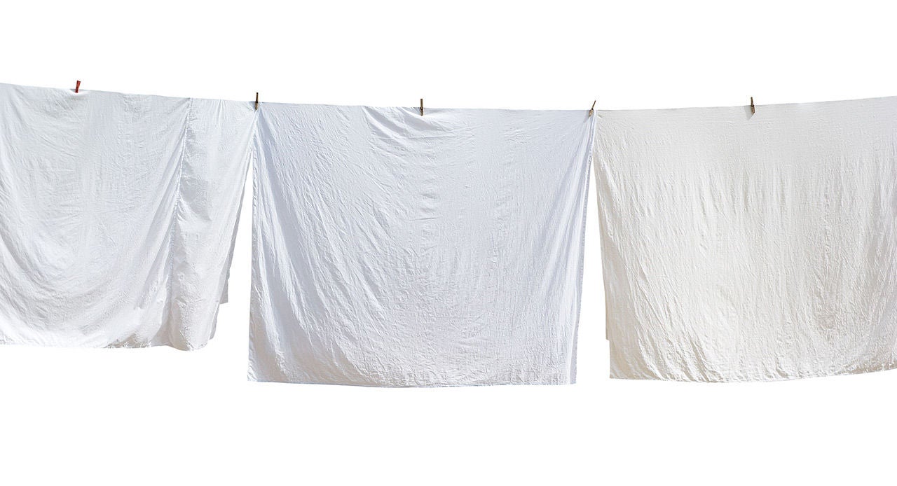 Três lençóis brancos pendurados no varal após aprender como tirar mancha amarela de roupa branca com este tutorial.