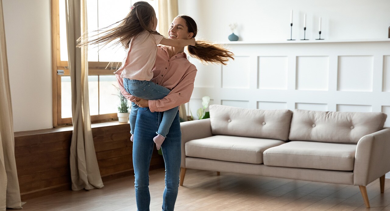 Mulher dançando com a filha no meio da sala após o robô aspirador tirar o grosso da sujeira do ambiente