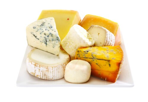 Uma tábua com vários tipos de queijo, incluindo opções macias e duras, alguns com veios azuis, exibindo diferentes texturas e cores.