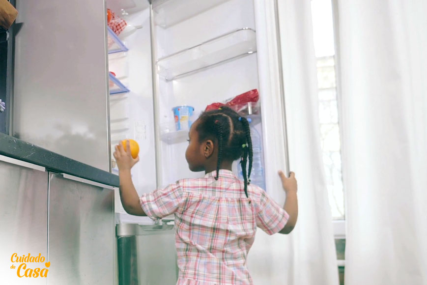 Criança pegando uma fruta da geladeira limpa e organizada