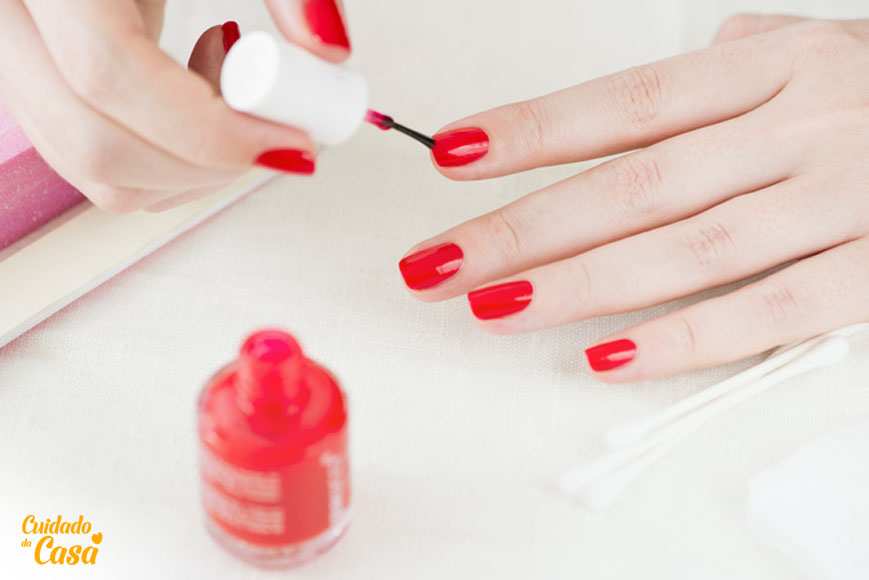 Mulher de mão branca fazendo a unha e pintando de esmalte vermelho