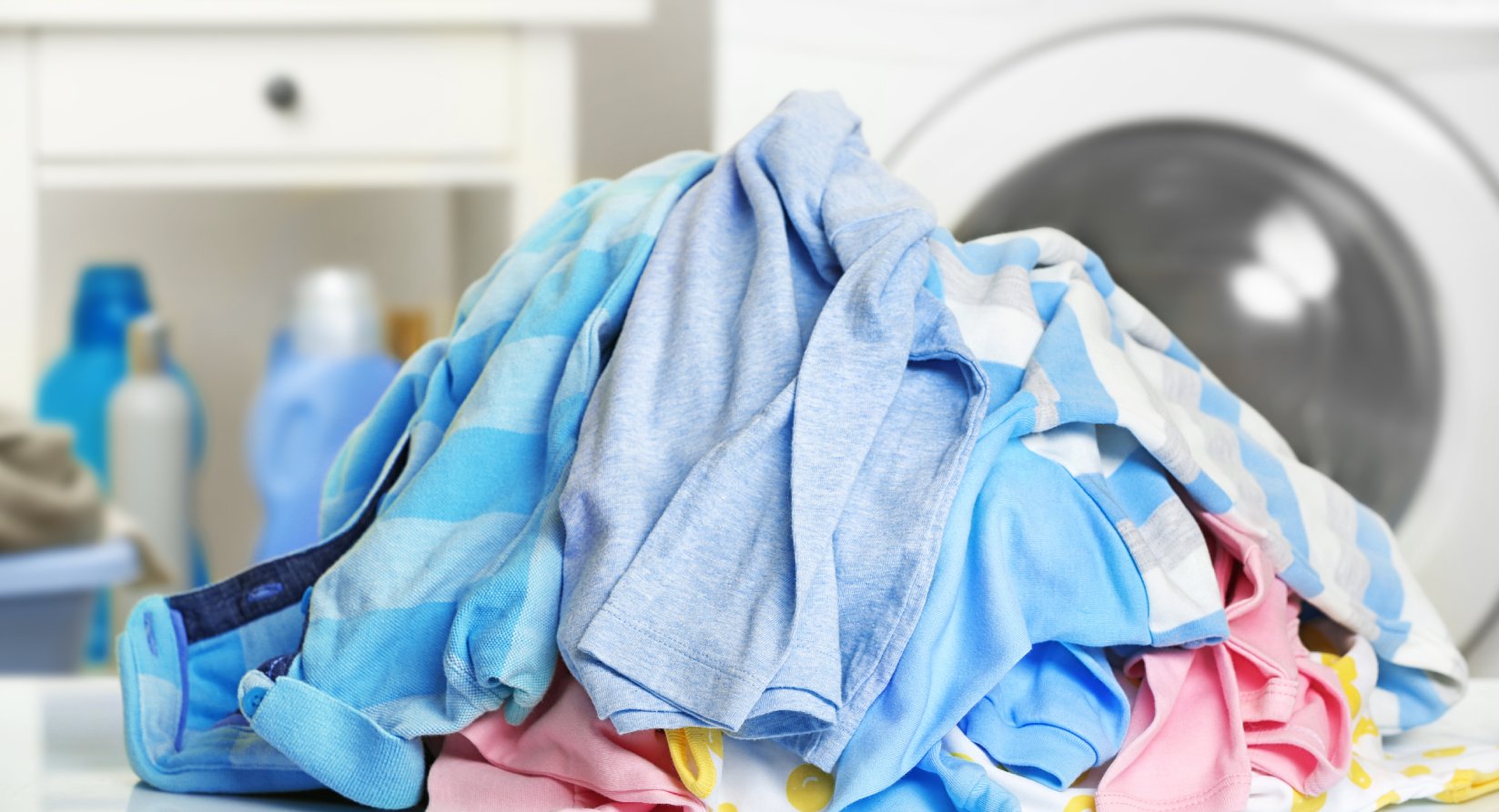Pilha de roupa suja sobre uma bancada, com uma máquina de lavar roupa ao fundo